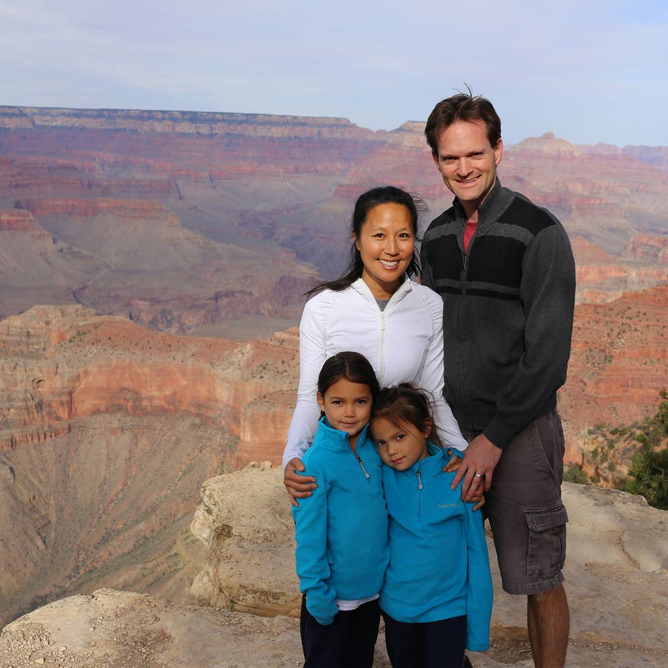 A woman, man and two young girls pose in front of the Grand Canyon wearing light jackets.