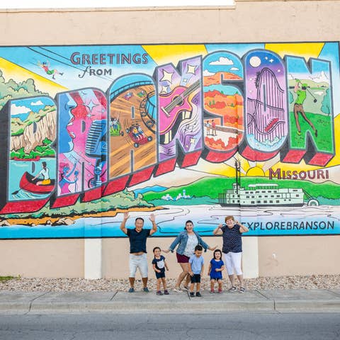 Family in front of Greetings from Branson sign near Holiday Hills Resort.