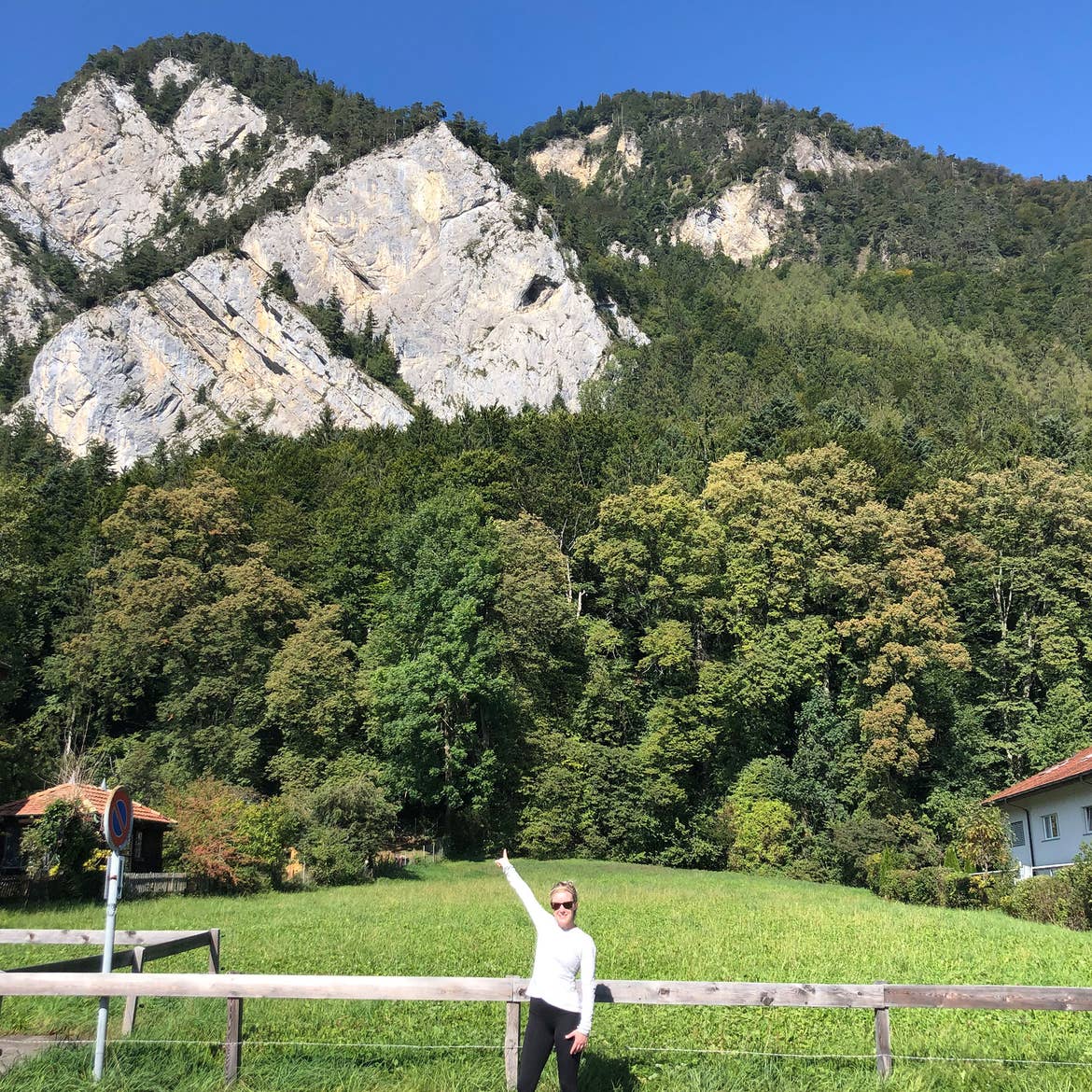 Co-author, Molly, wears a white shirt and black shorts while posing in front of a mountain in Switzerland.