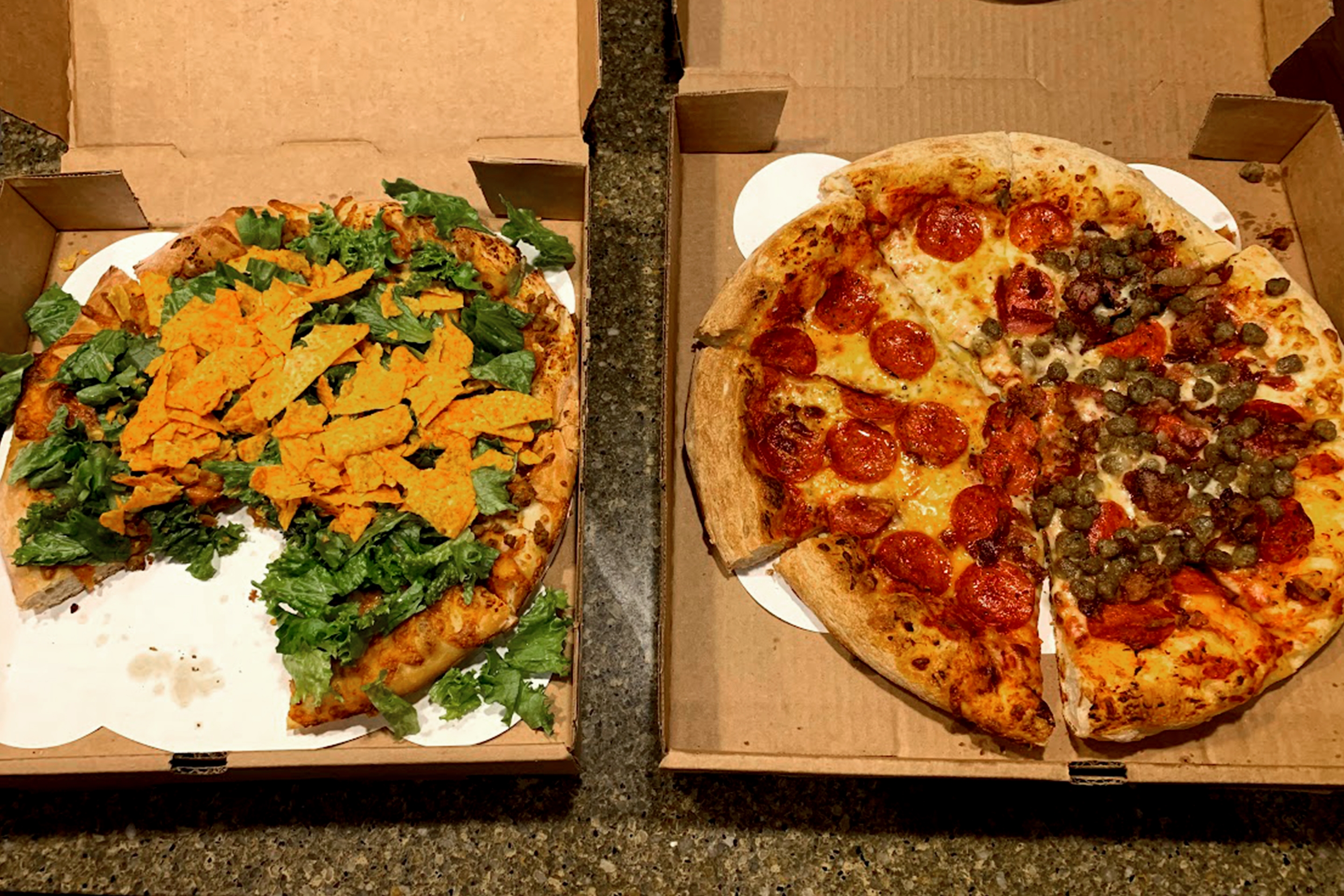 Two pizzas in boxes displayed on a table with various toppings.