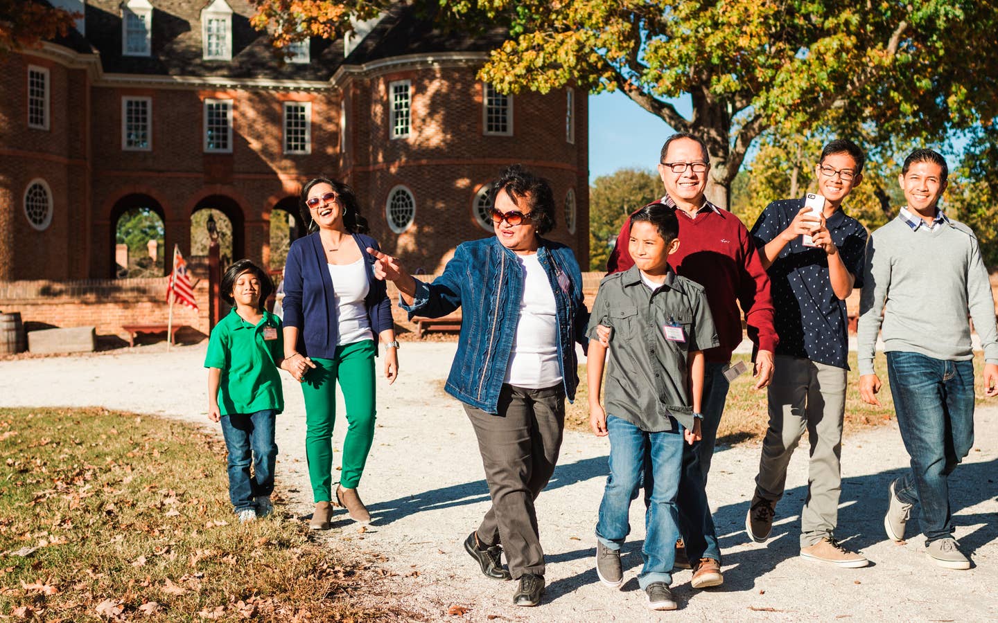 Several men, women and children walk outdoors around Colonial Williamsburg dressed in fall apparel.