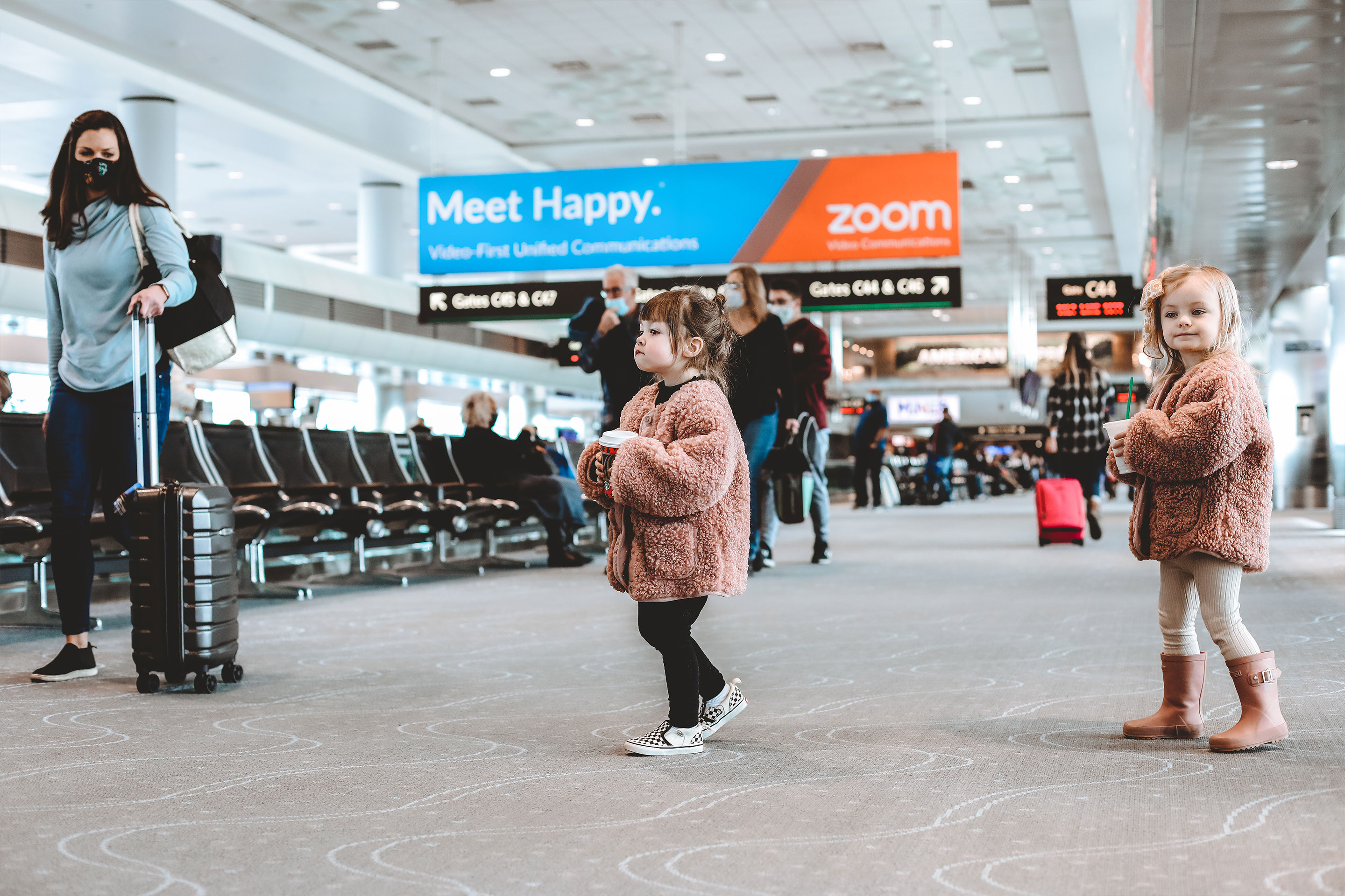 Featured contributor, Mia St. Clair's daughter (middle) and cousin walking in an airport terminal wearing pink fluffy coats.