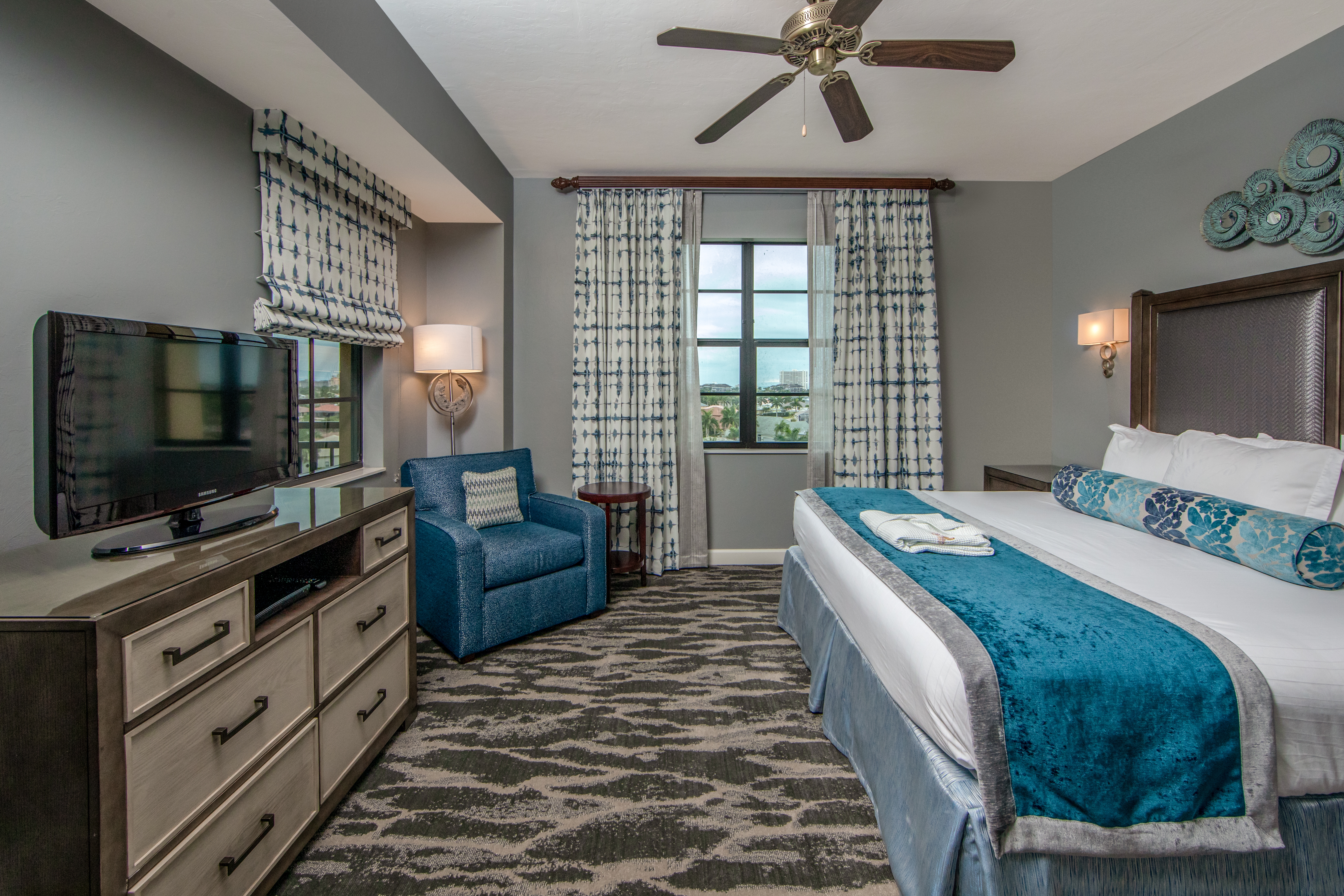 Bedroom with king bed, flat screen TV, large window, and seating area in a three-bedroom villa at Sunset Cove Resort in Marco Island, Florida