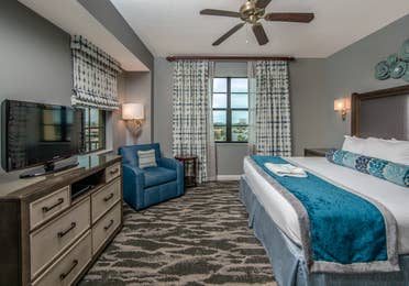 Bedroom with king bed, flat screen TV, large window, and seating area in a three-bedroom villa at Sunset Cove Resort in Marco Island, Florida