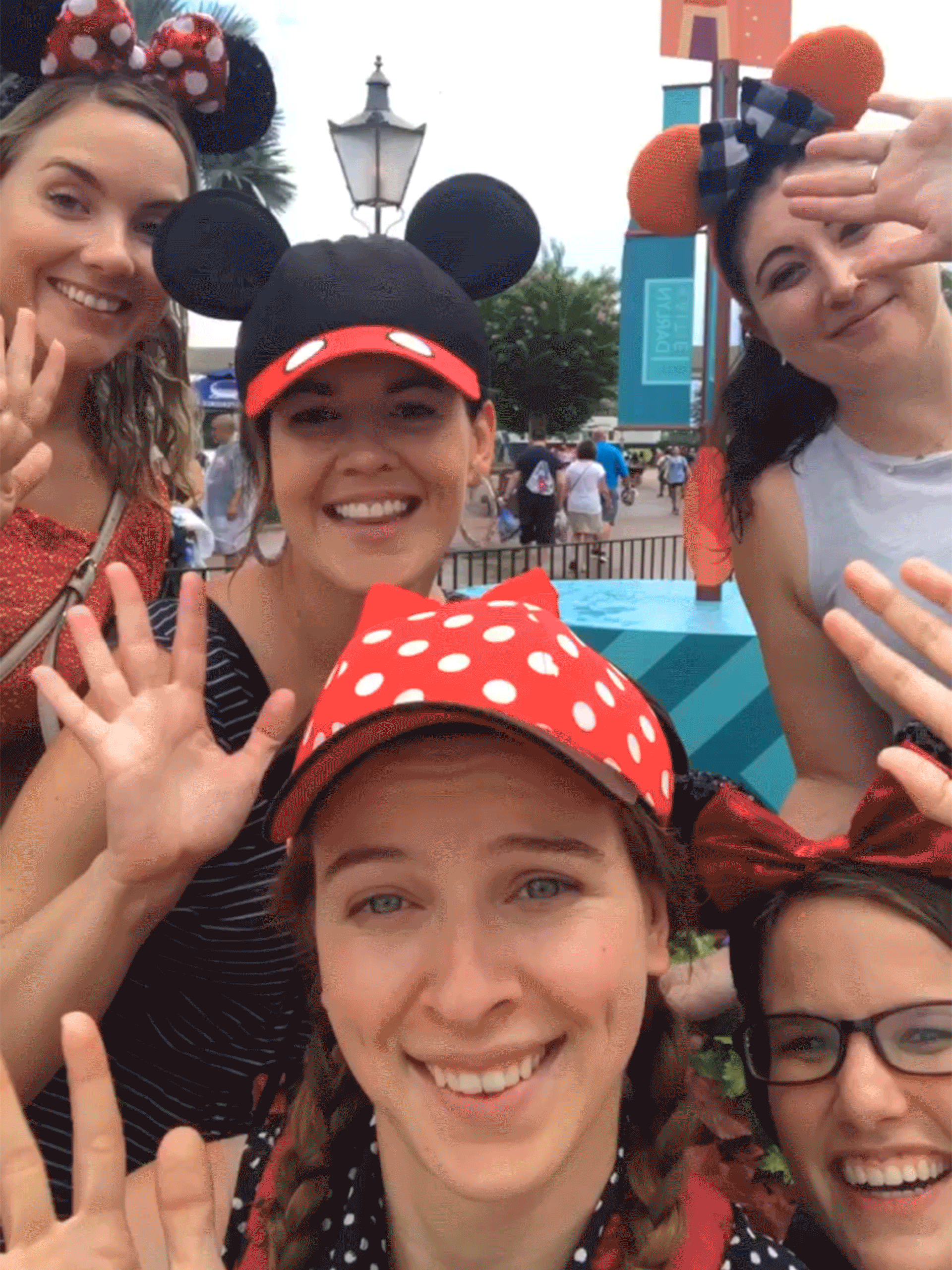 Five caucasian women wearing Mickey & Minnie ears wave at the camera.