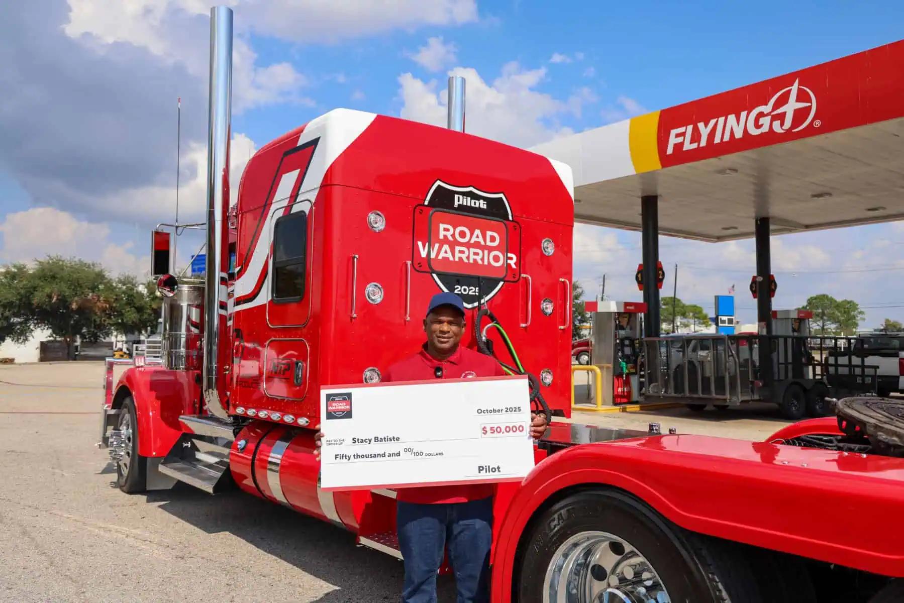 Pro truck driver standing in front of a red bobtail truck holding a giant check