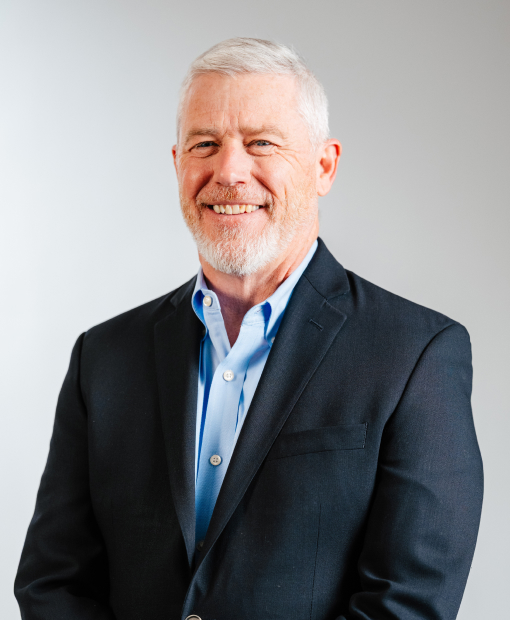 Ted Brennan smiling, wearing a dark blazer and light blue shirt, professional headshot