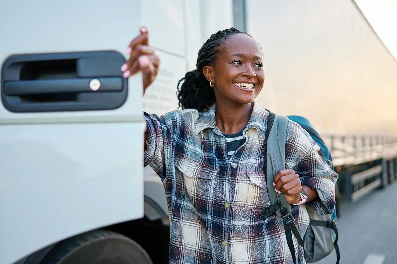 A happy pro driver getting out of her semi truck with a backpack on her back