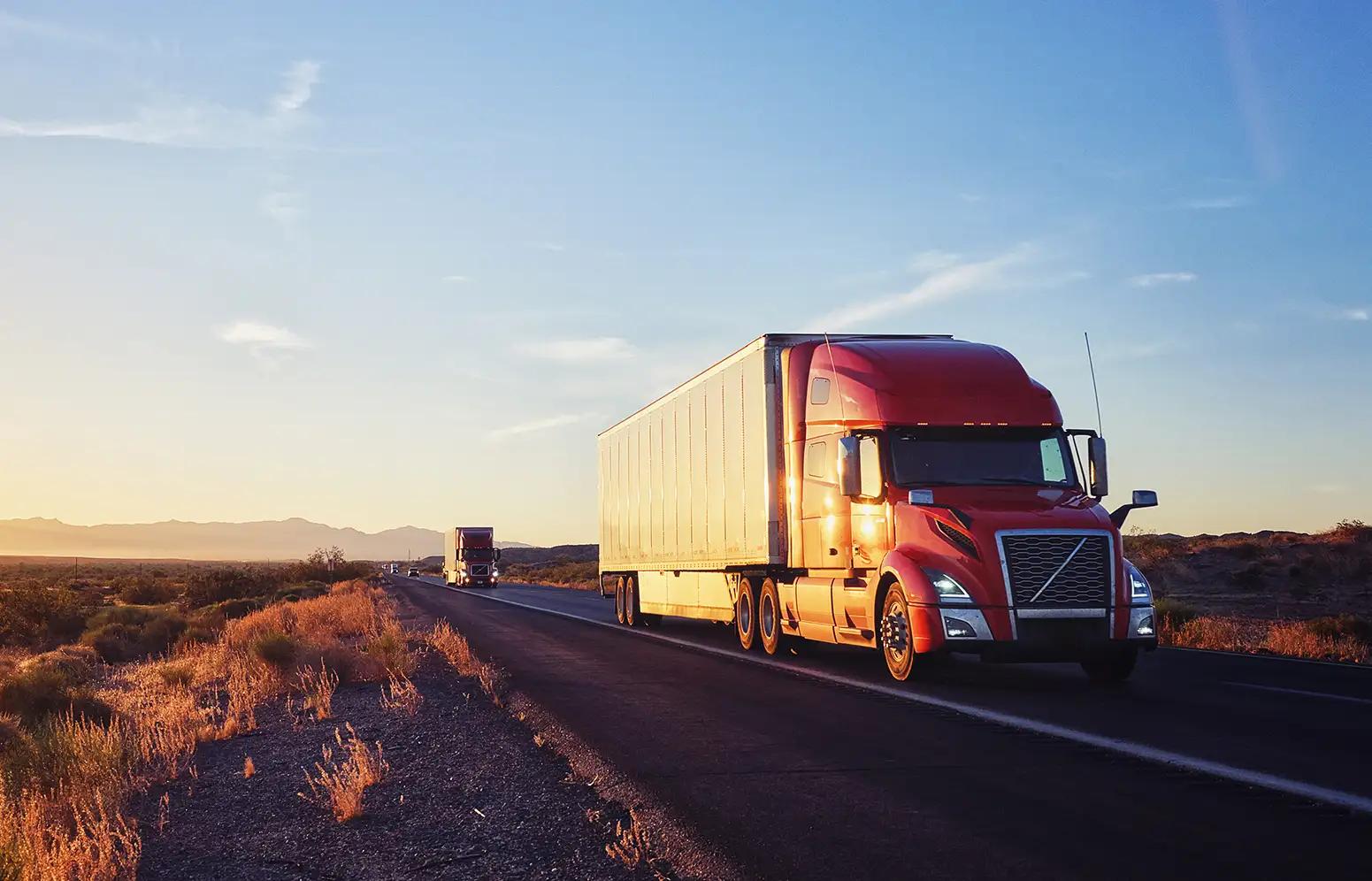 A semi-truck driving down a desert highway with another semi-truck following behind