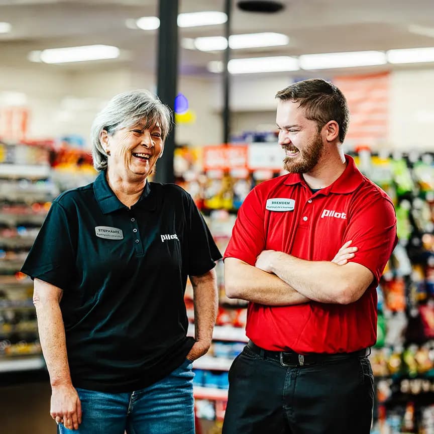 Two Pilot employees in uniform chatting inside a store aisle with products in the background