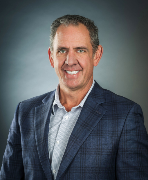 Professional headshot of Derek Panfil, wearing a navy blue plaid blazer and striped dress shirt, smiling against a gray studio background