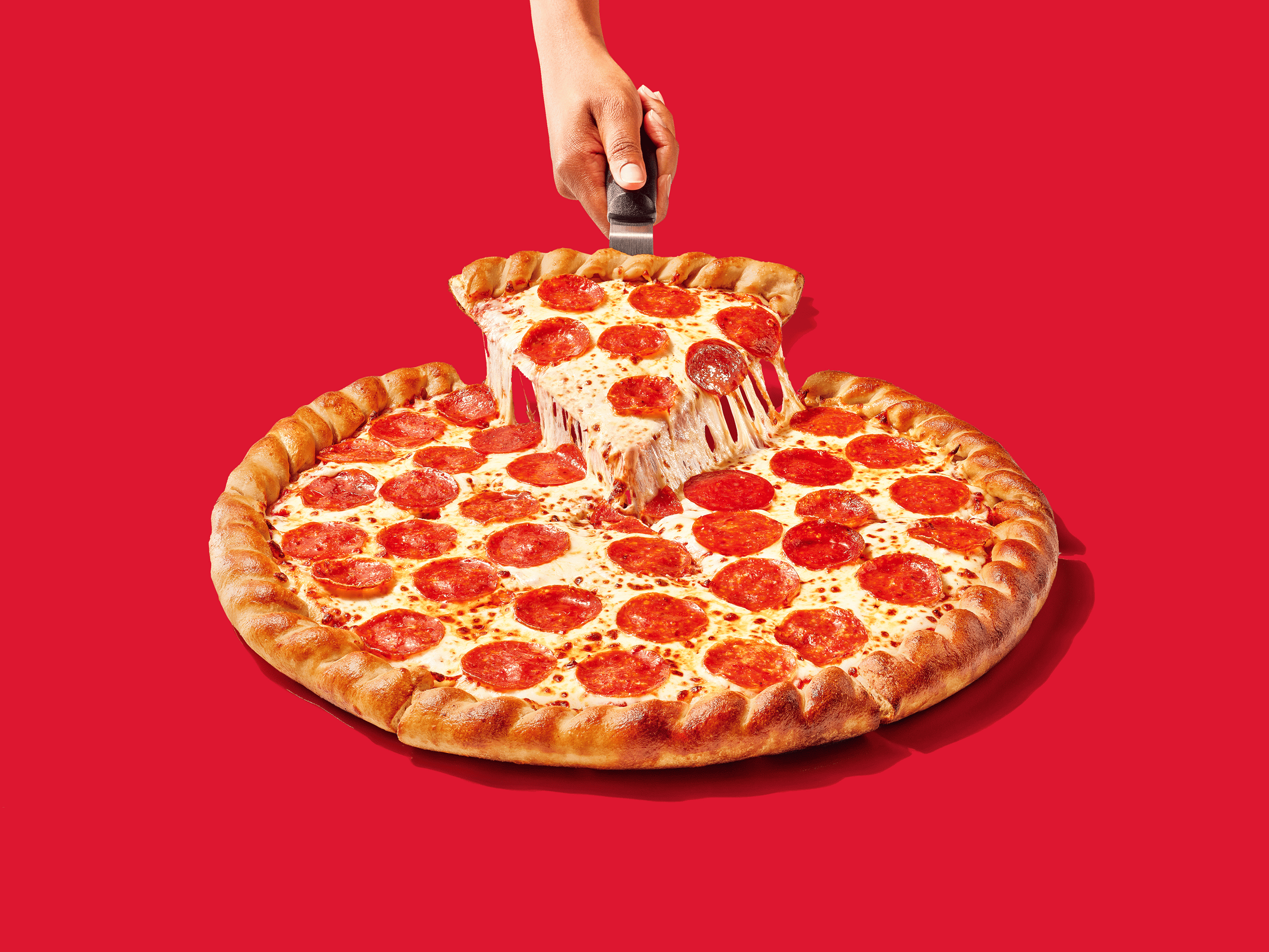 Whole pepperoni pizza with a slice being pulled out on red background
