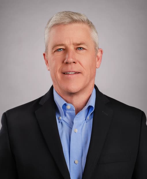 Ted Brennan smiling, wearing a dark blazer and light blue shirt, professional headshot