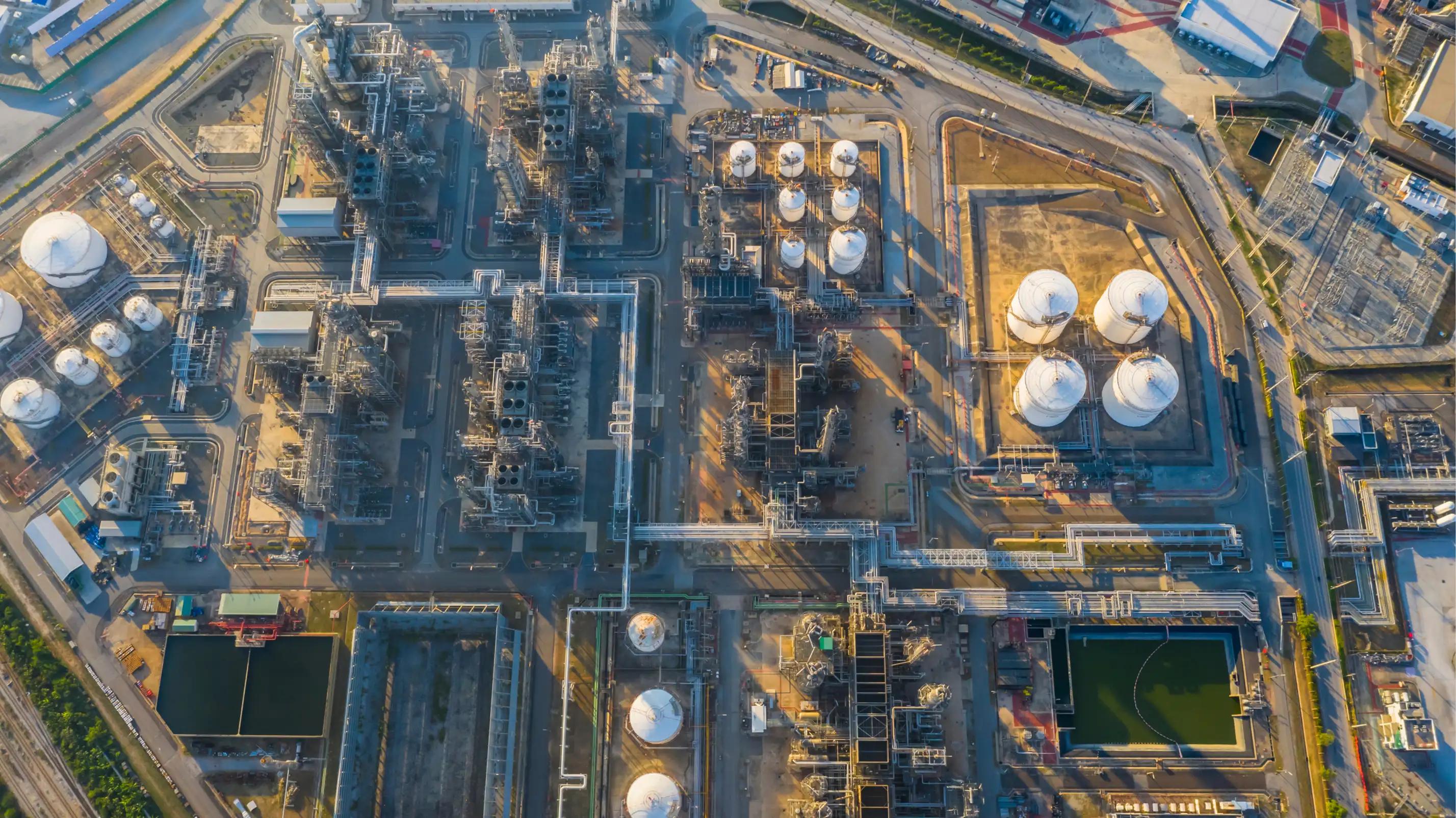 Aerial view of a large petrochemical processing facility featuring multiple white spherical storage tanks, extensive pipeline networks, industrial processing units, and wastewater treatment ponds