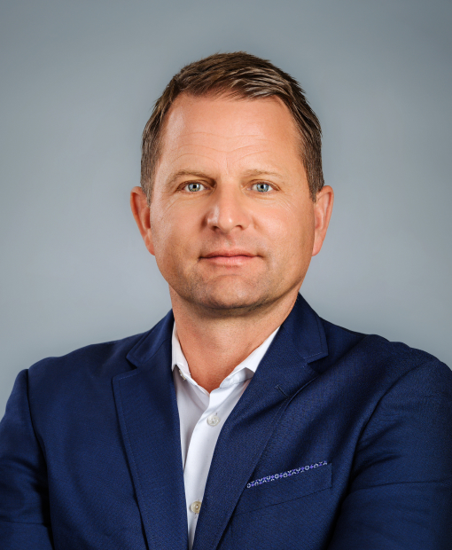 Professional headshot of Andy Lupo, a man with short dark hair and blue eyes wearing a navy blue blazer and white shirt, photographed against a gray background