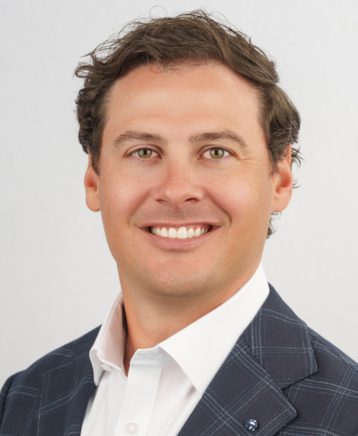 Professional headshot of Sam Edgmon, a smiling man with brown hair, wearing a navy plaid blazer over a white dress shirt, photographed against a light gray background