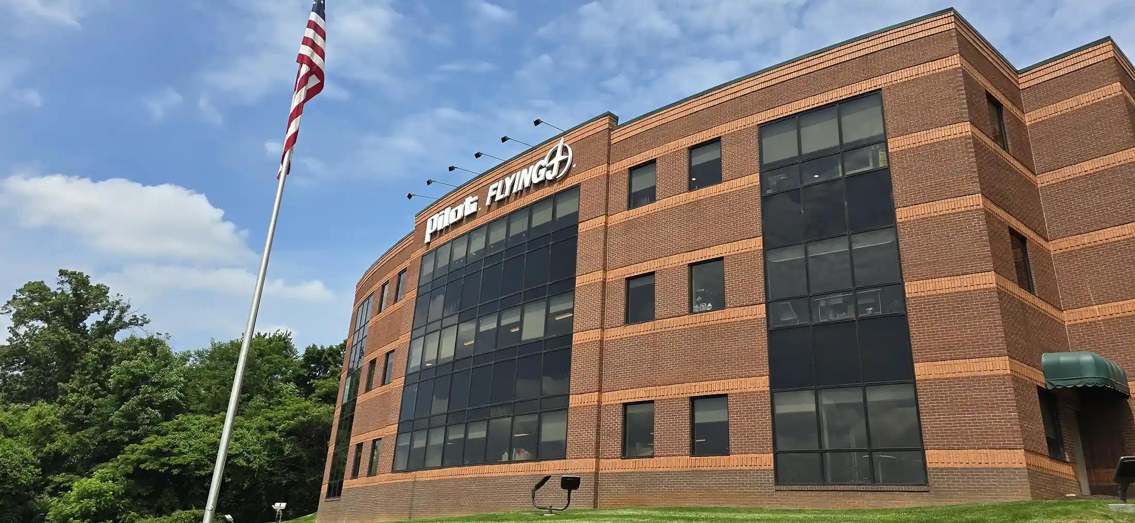 Pilot Company corporate headquarters, a multi-story brick office building with large glass windows and the Pilot Flying J logo displayed on the exterior, with an American flag in the foreground