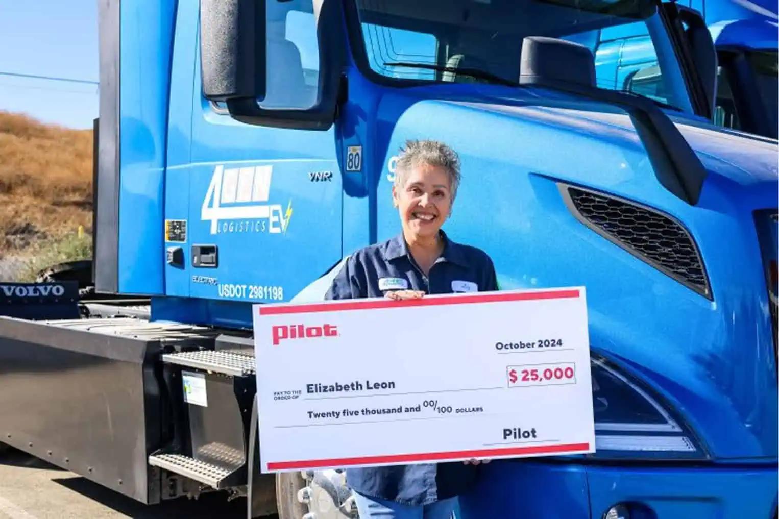 Woman stand in front of a blue semi truck holding a giant check