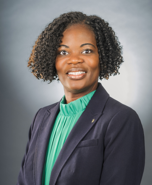 Professional headshot of Jocelyn Caldwell wearing a dark navy blazer over a teal/green ruffled blouse, smiling against a neutral gray background