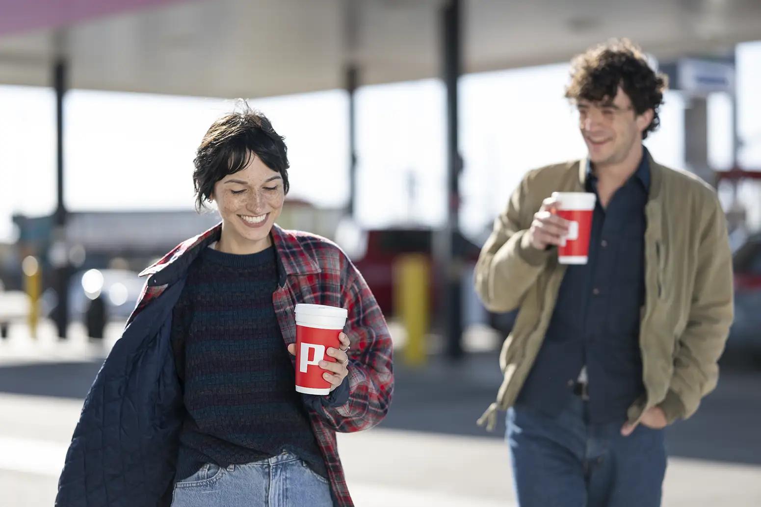 Two people on road trip walking out of the Pilot with drinks in their hands