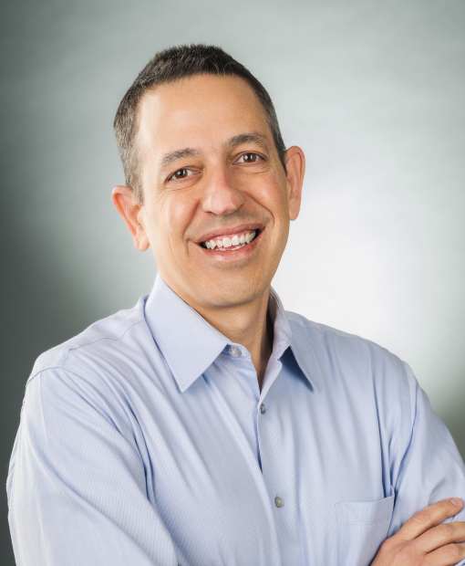 Headshot of a smiling Sean Marrero, wearing a light blue button-down shirt, arms crossed, against a soft gray background