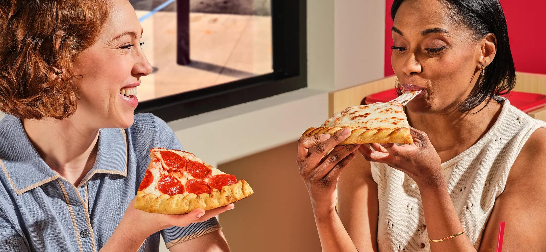 A woman and a man inside a vehicle eating two slices of pepperoni pizza