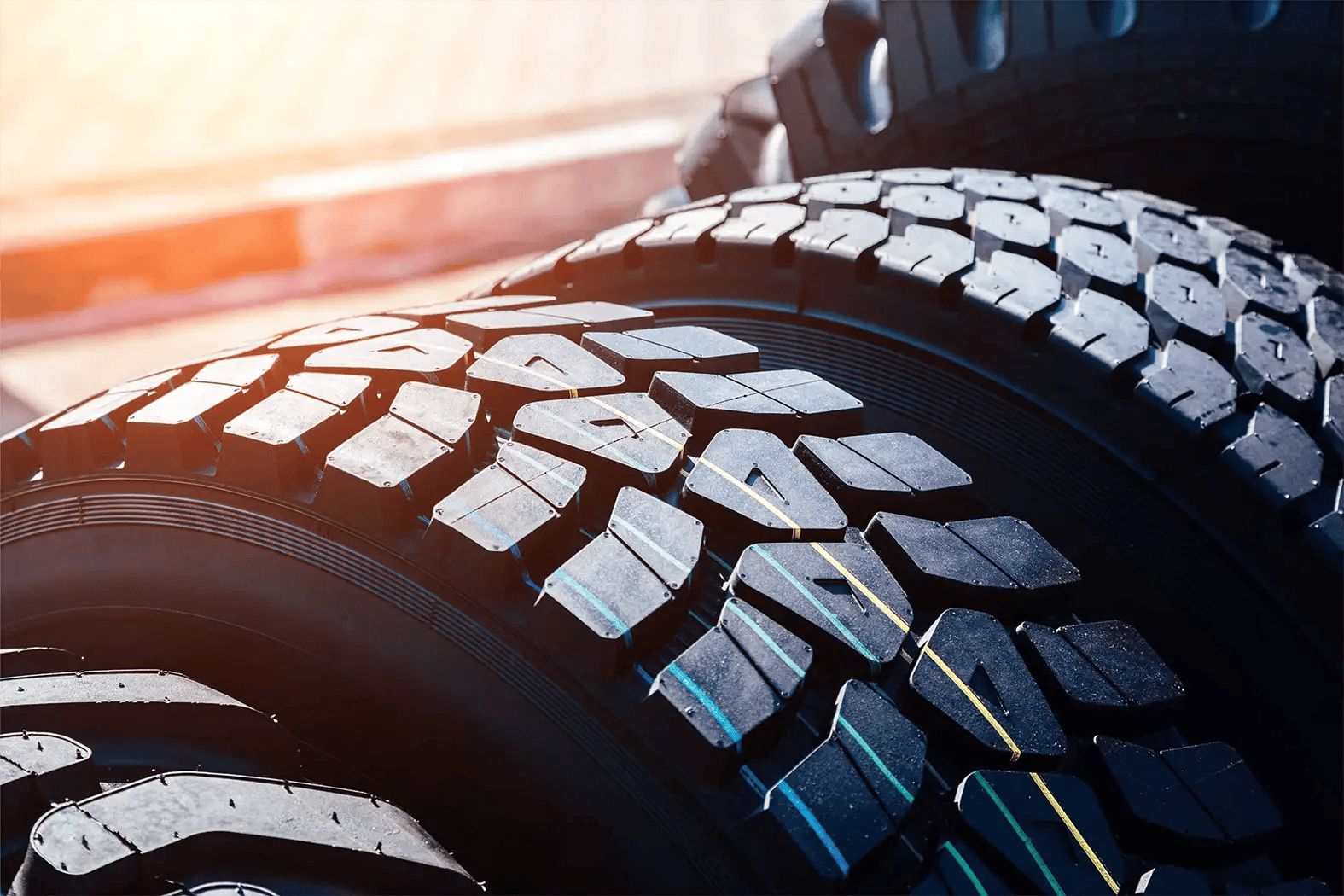 Close-up view of new heavy-duty truck tire tread showing aggressive block pattern with blue and yellow stripe wear indicators on stacked tires