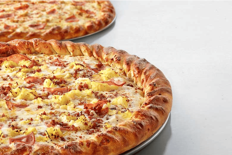 Two large pizzas with twisted braided crusts topped with scrambled eggs, crumbled bacon, diced ham, and melted cheese â€” a breakfast-style pizza
