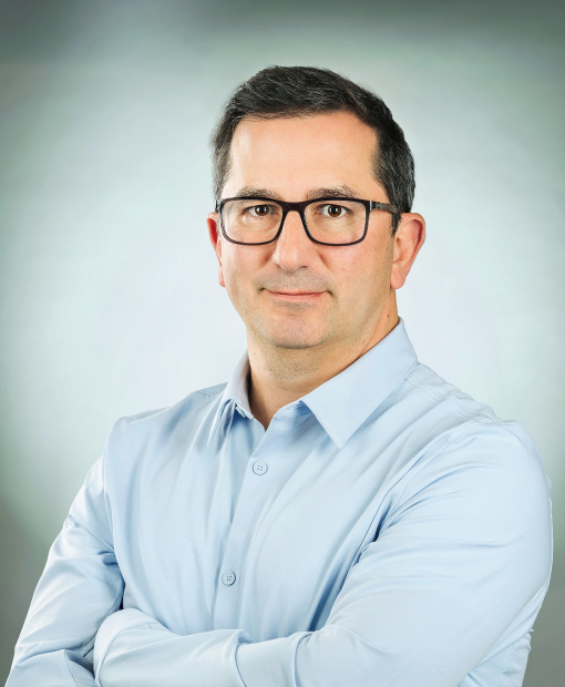 Professional headshot of Jorge Valdes with glasses on, wearing a light blue dress shirt with arms crossed, against a soft gray background