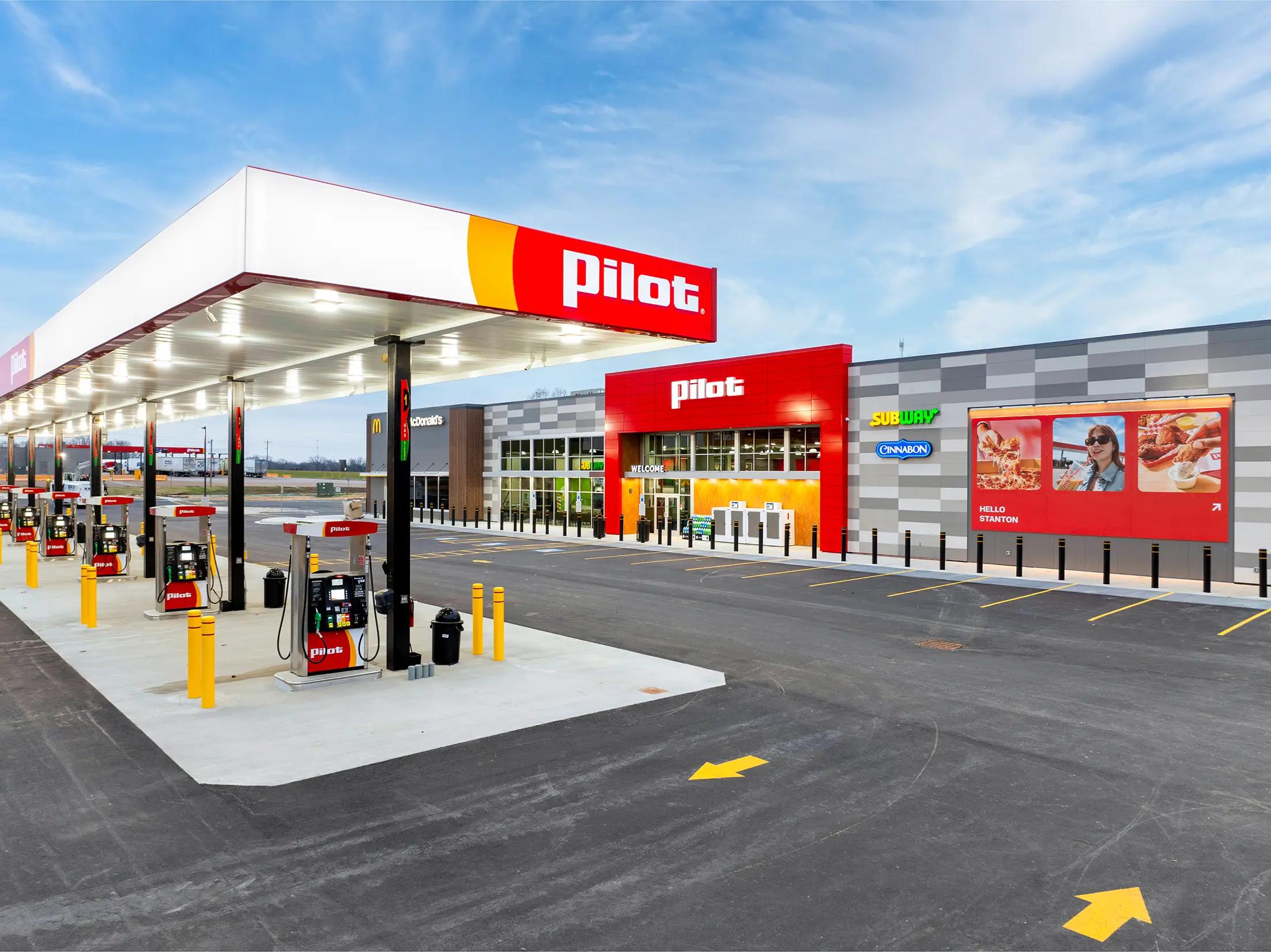 Exterior view of a Pilot Travel Center featuring a covered fuel canopy with multiple gas pumps in the foreground and a large retail building housing McDonald's, Subway, and Cinnabon restaurants