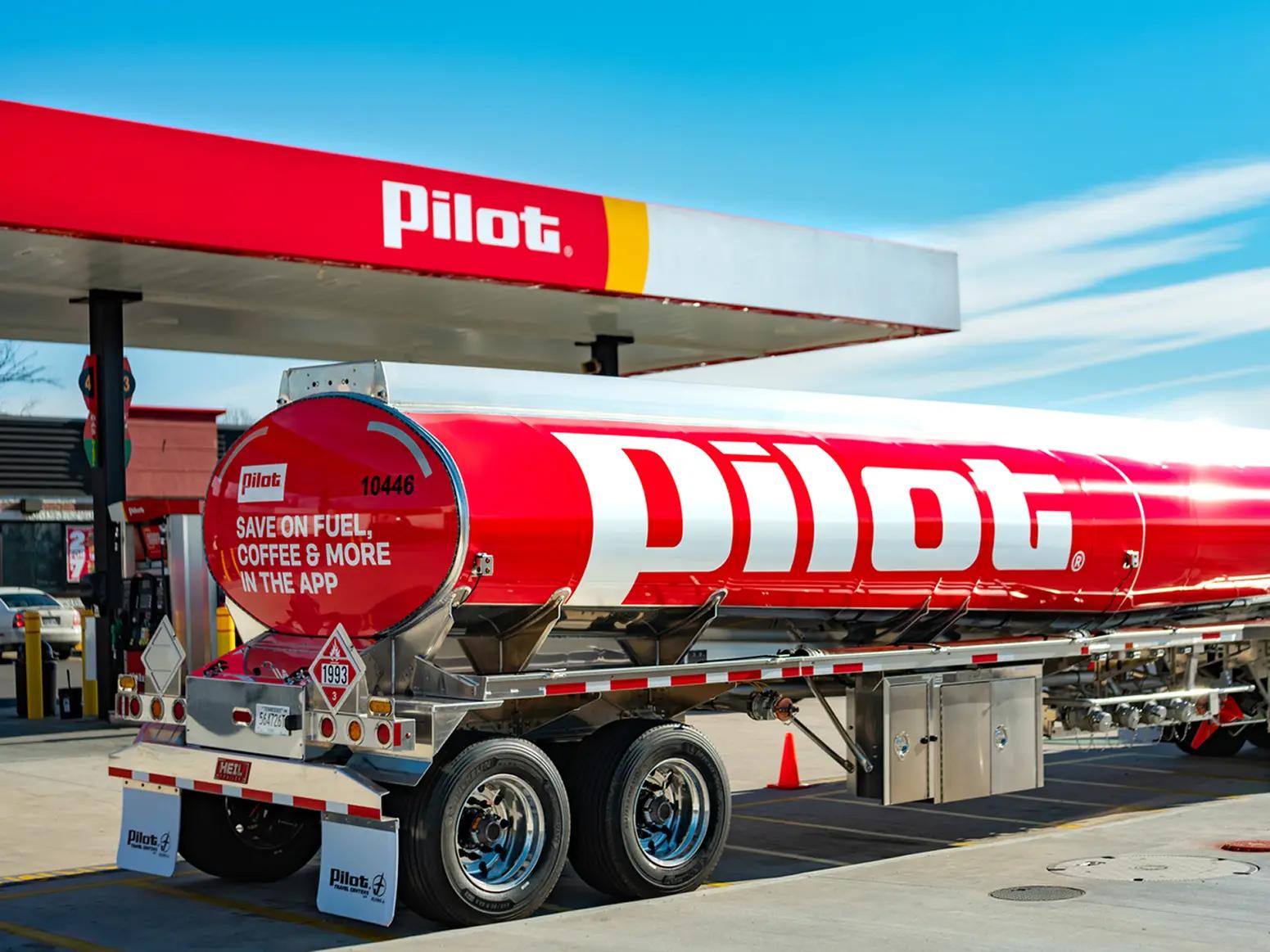 A red Pilot-branded fuel tanker trailer parked under a Pilot Travel Center fuel canopy, with promotional text on the rear reading 'Save on Fuel, Coffee & More in the App'