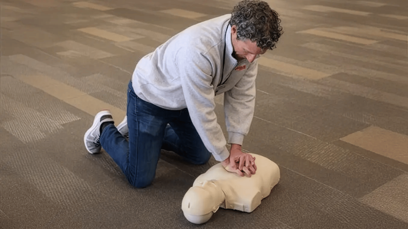 Man kneeling on the floor performing chest compressions on a CPR training manikin