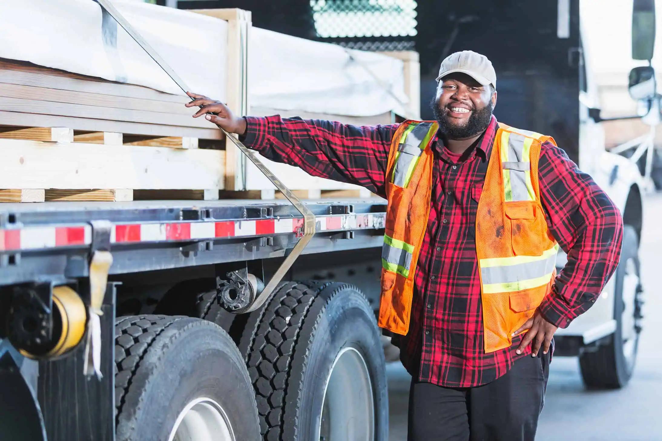 A worker in an orange high-visibility safety vest standing alongside a large semi truck