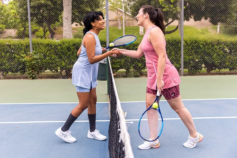 Two women playing tennis on a hard court