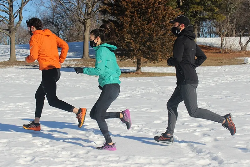 Three runners running on the snow in a field