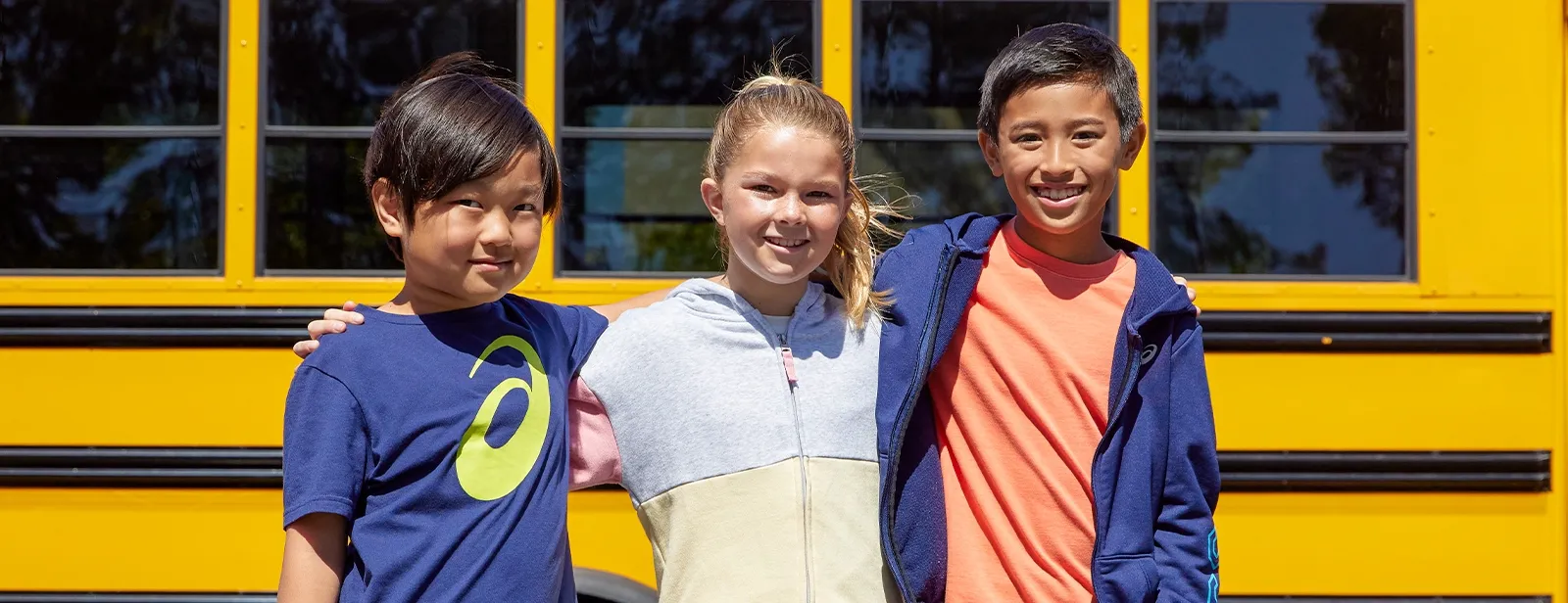 Three kids infront of a school bus posing for a picture