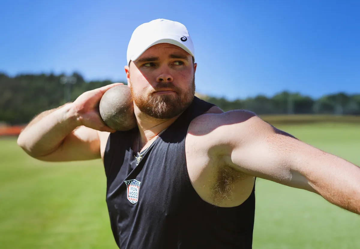 ASICS Athlete Payton Otterdahl wearing a white hat and black tank top about to throw the shot put