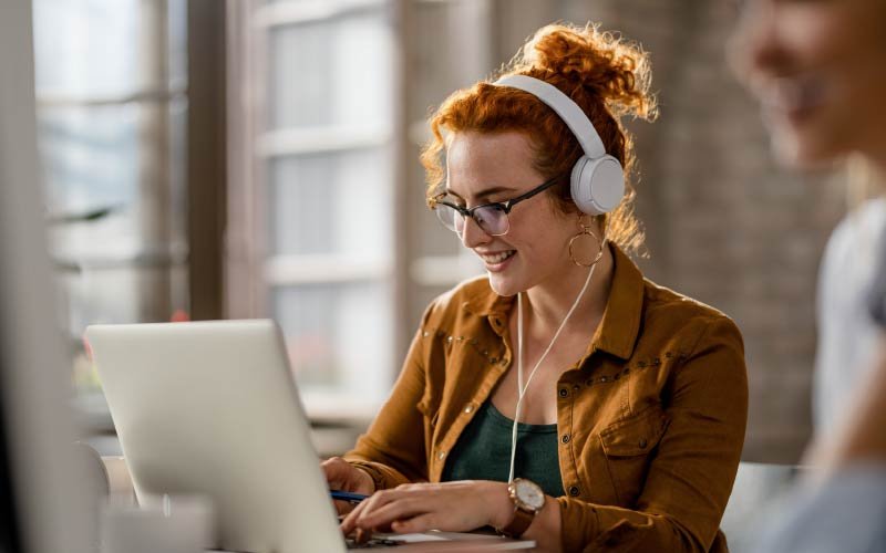 A woman wearing headphones listening at her laptop.