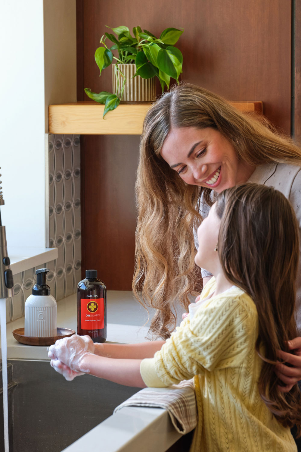 Mother helping her child wash her hands at the sink with doTERRA On Guard Foaming Hand Wash