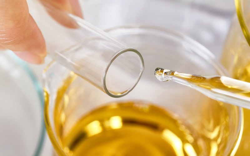 A drop of essential oil falling from a glass pipette into a beaker.
