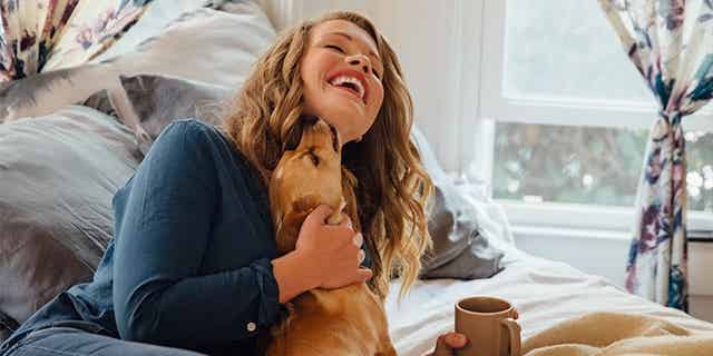 Woman laughing as she plays with her dog at home
