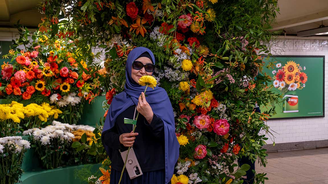 Woman with flower giveaway in front of Flower Flash installation for Zyrtec along with two-sheet poster on wall behind