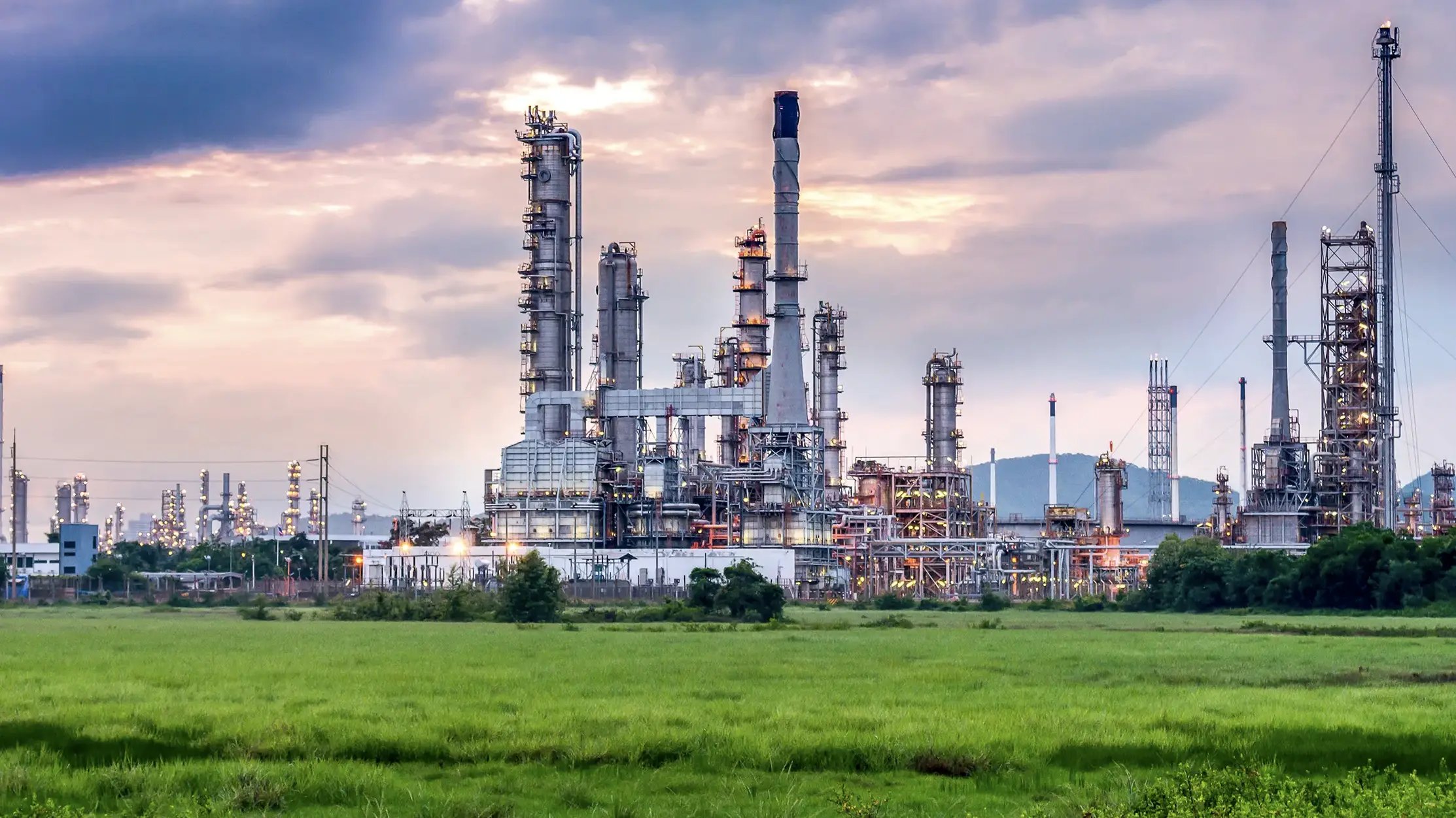 A field of bright green grass with a powerplant in the background.