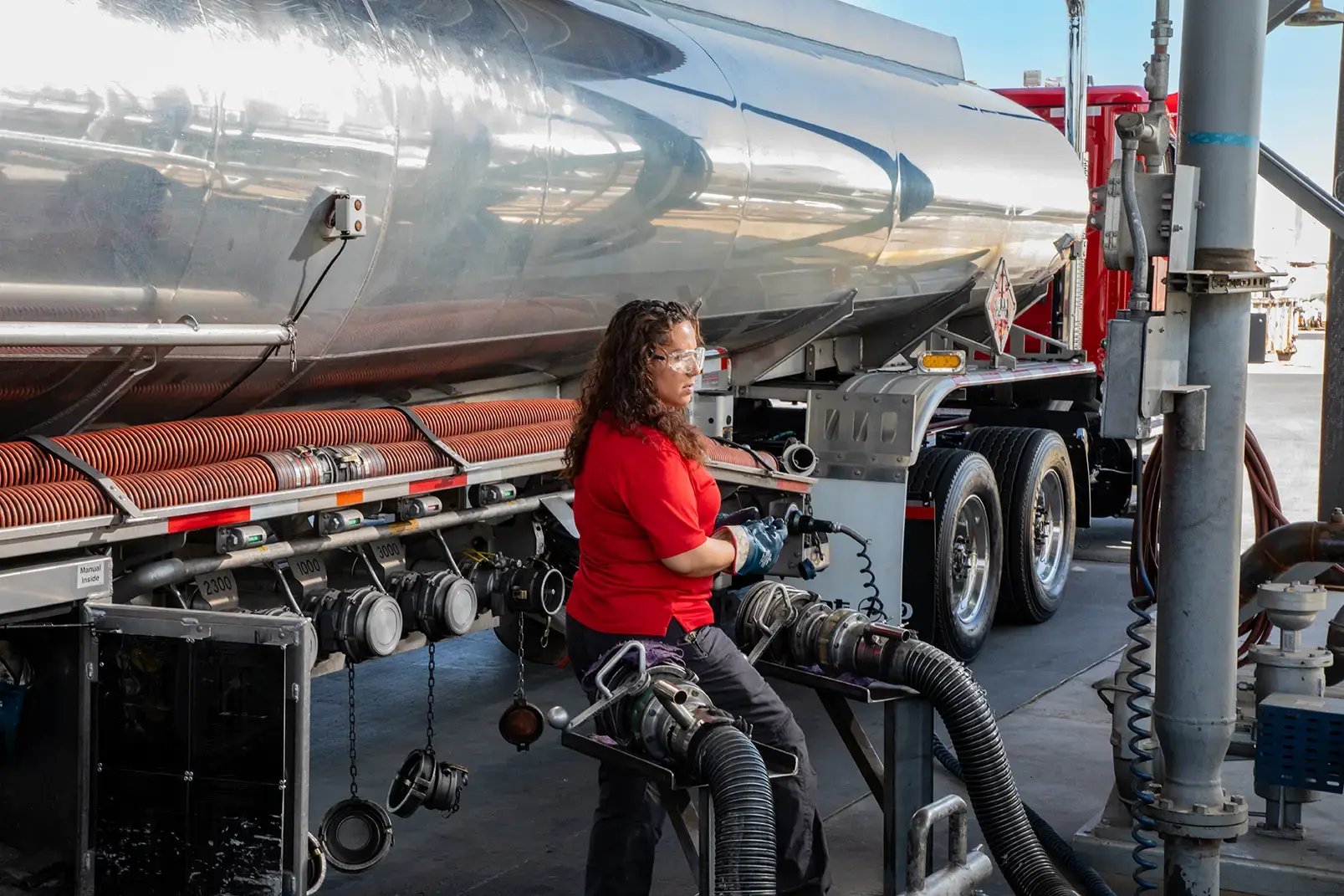 A person is pumping fuel from a tank on a truck with a large hose.
