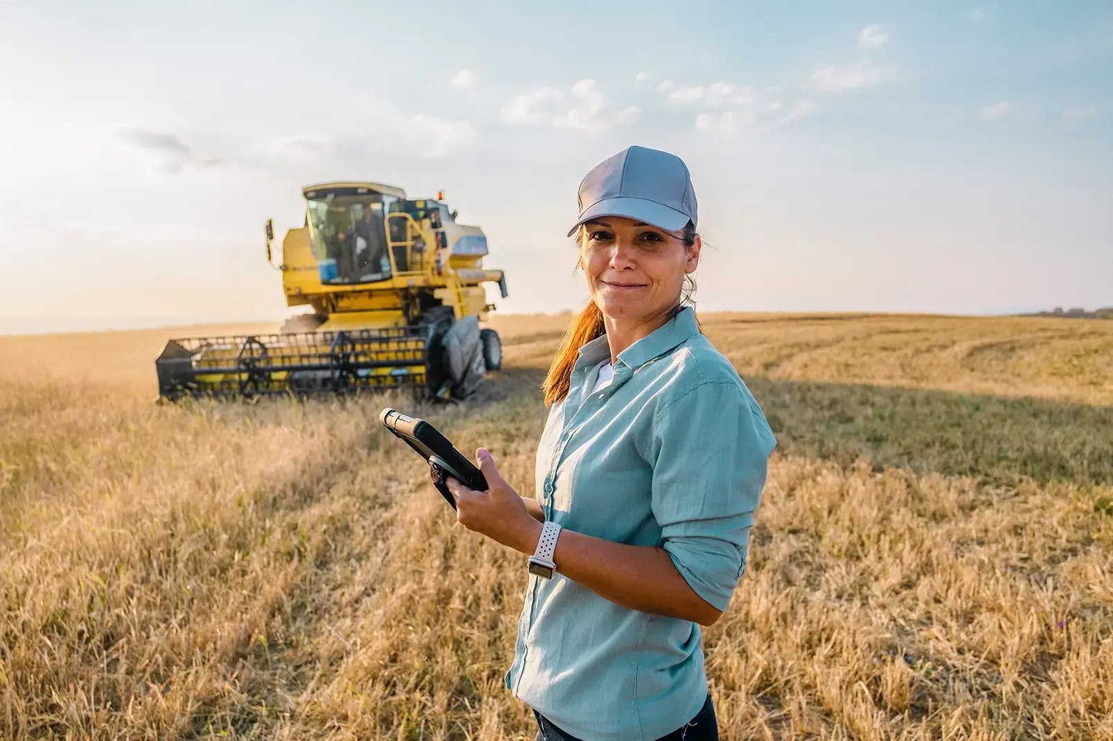 A person stands in a field of grain while holding a tablet.