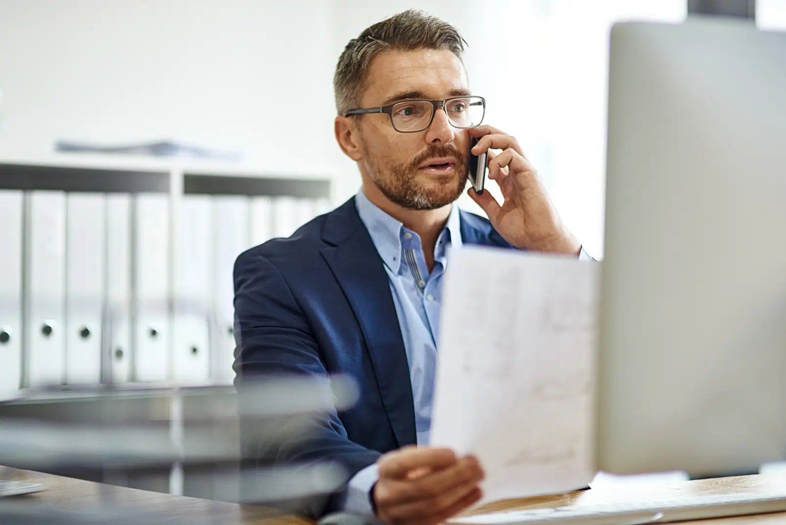 Person on phone looking at computer monitor.