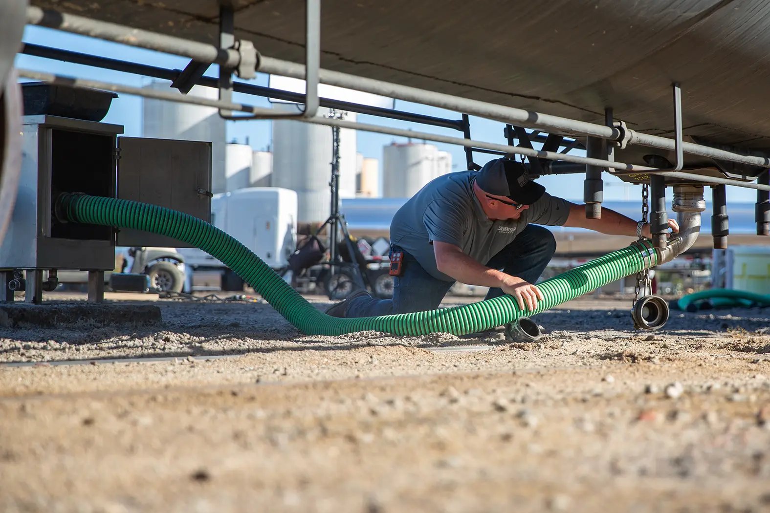 A person is hooking up hoses underneath a tank on a truck.