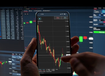 phone showing tastyfx platform and a computer monitor in the background
