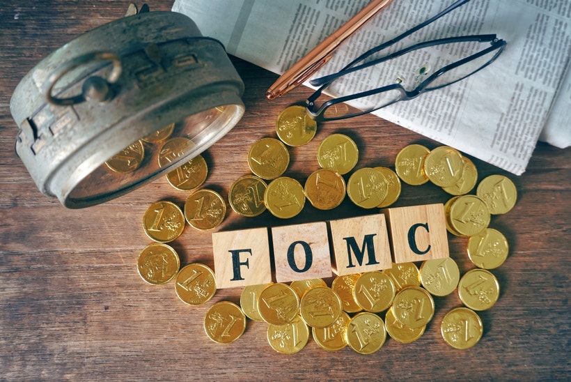 Blocks spelling FOMC on a desk with gold coins