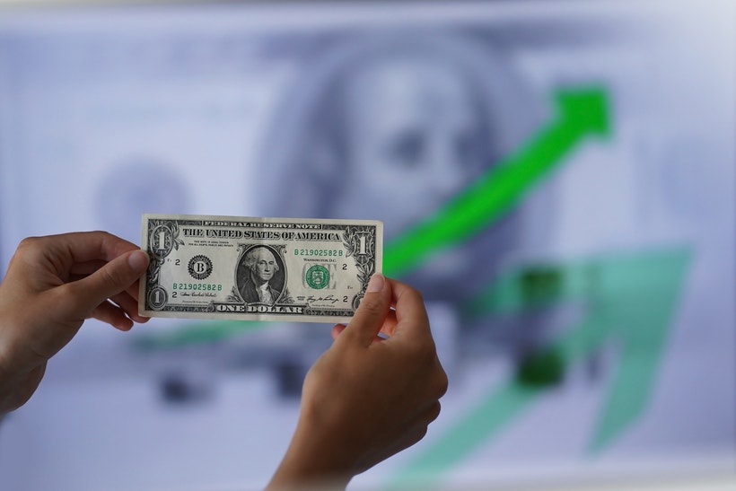 US dollar being held in front of chart with green arrow pointing up